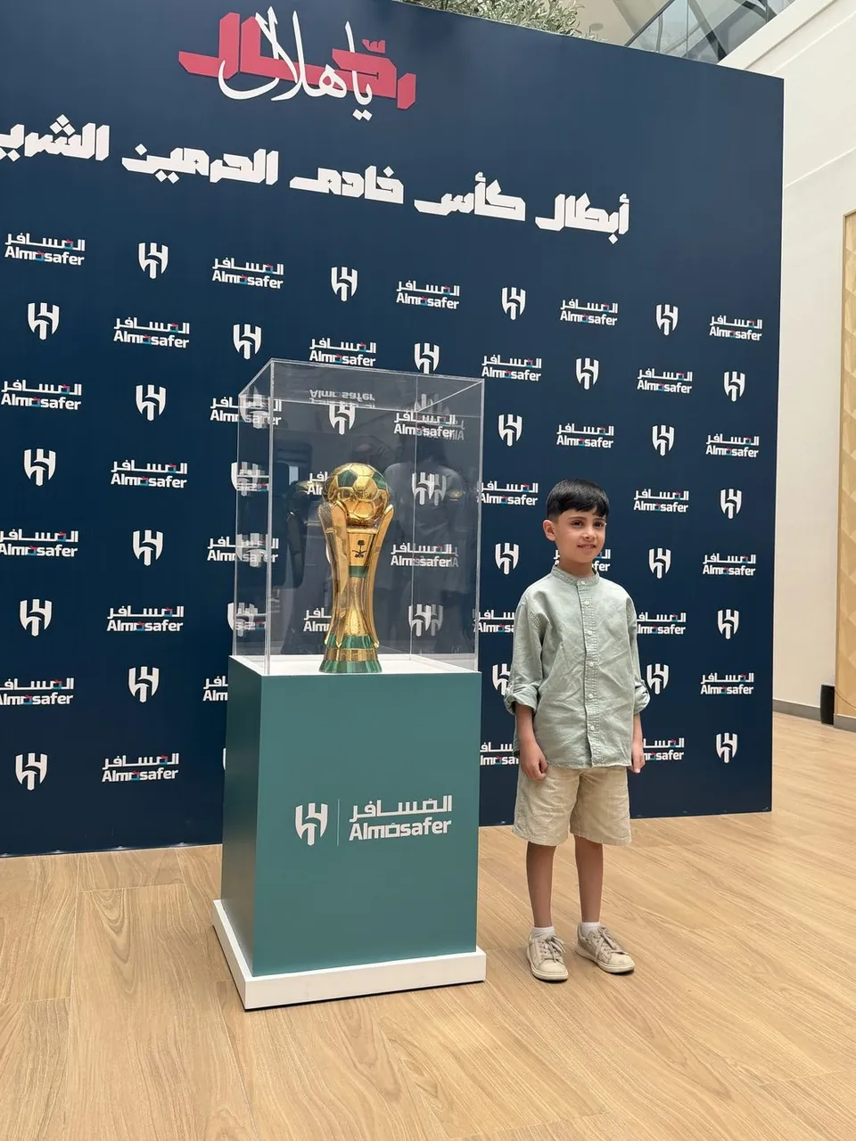 Young fan with the trophy at the Almosafer and Al Hilal backdrop